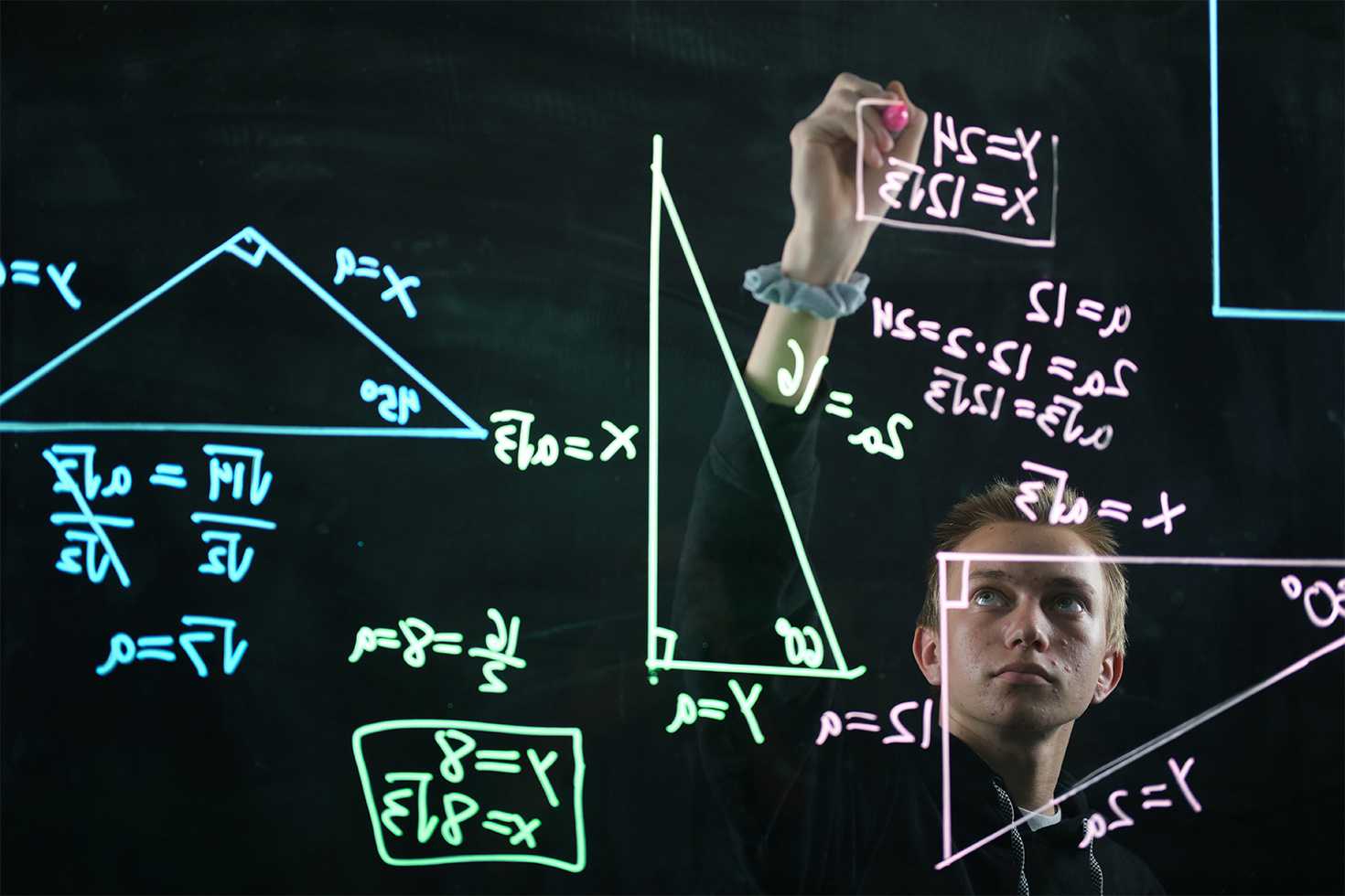 a student writing mathematical formulas on a glass board